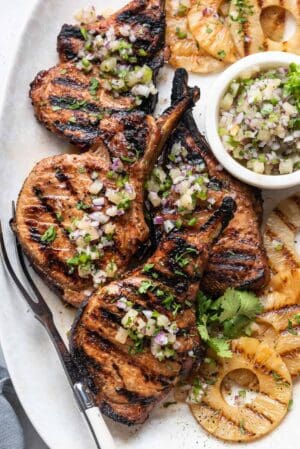 Grilled Pineapple Pork Chops on a platter with grilled pineapple and pineapple salsa.