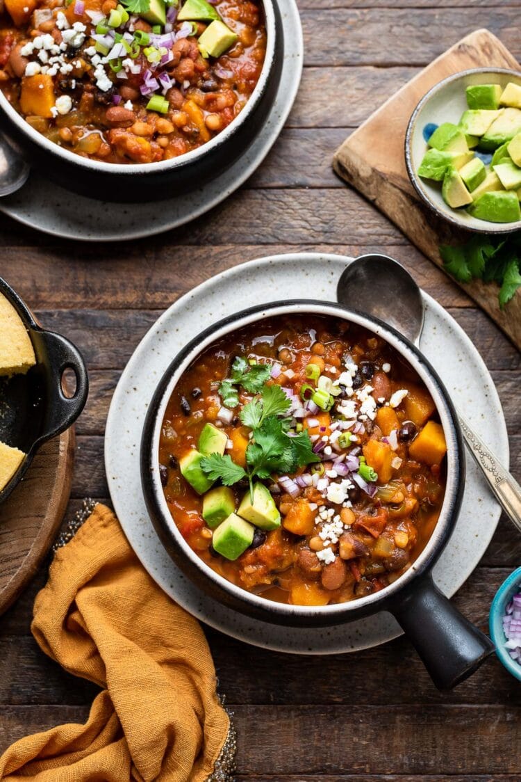 Kabocha Squash Chili in a bowl, garnished with avocado, cheese, red onion, green onion, and cilantro.